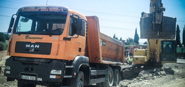 Excavadora giratoria cargando camión con los restos de una zanja en carretera