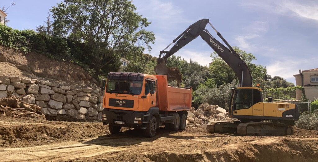 Excavadora y camión de Excavaciones Santa Bárbara junto a un muro de escollera en Granada